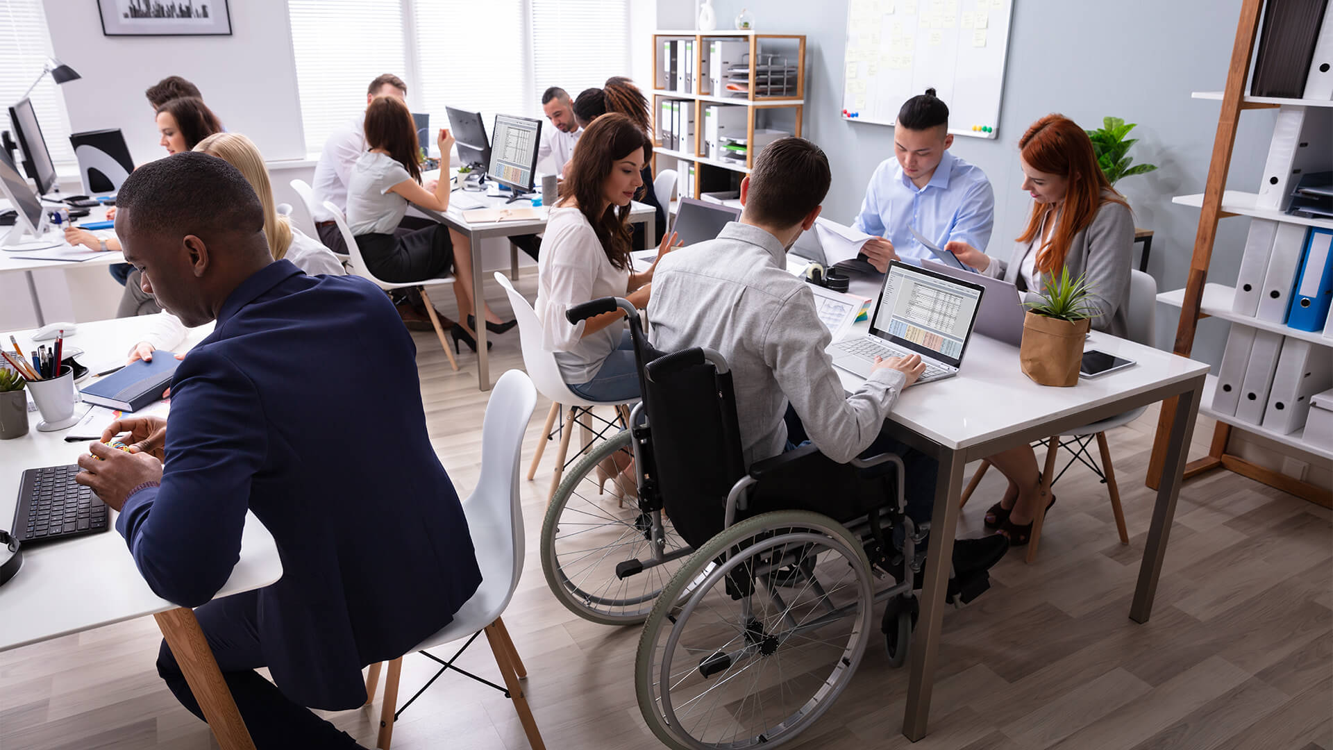 People working in an office, and the businessman closest to the camera using a wheelchair