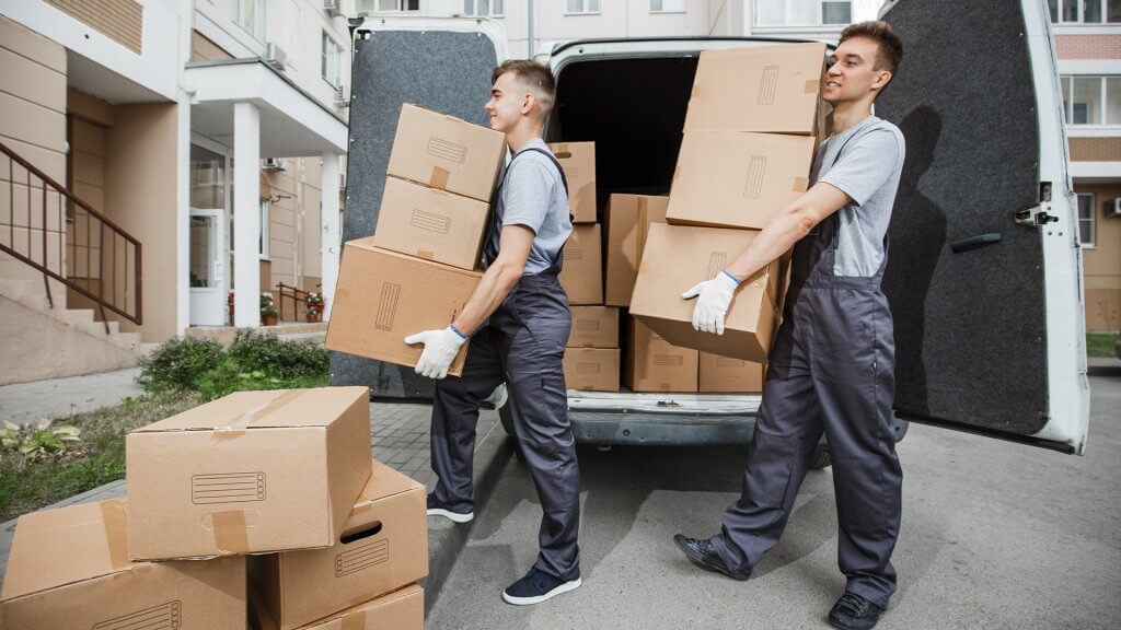 Two men working to move boxes into a house from their work van