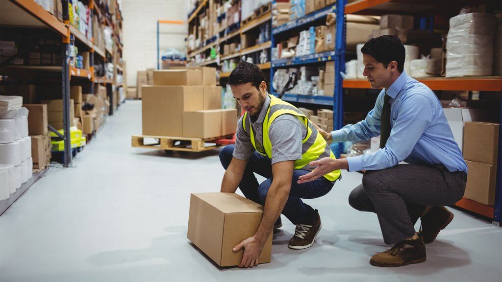 Employee in a warehouse being shown how to properly handle a heavy load