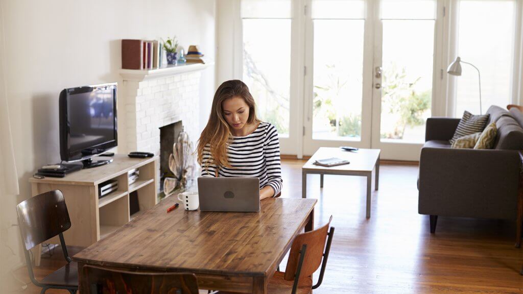 Woman working from home, using a laptop on her dining room table
