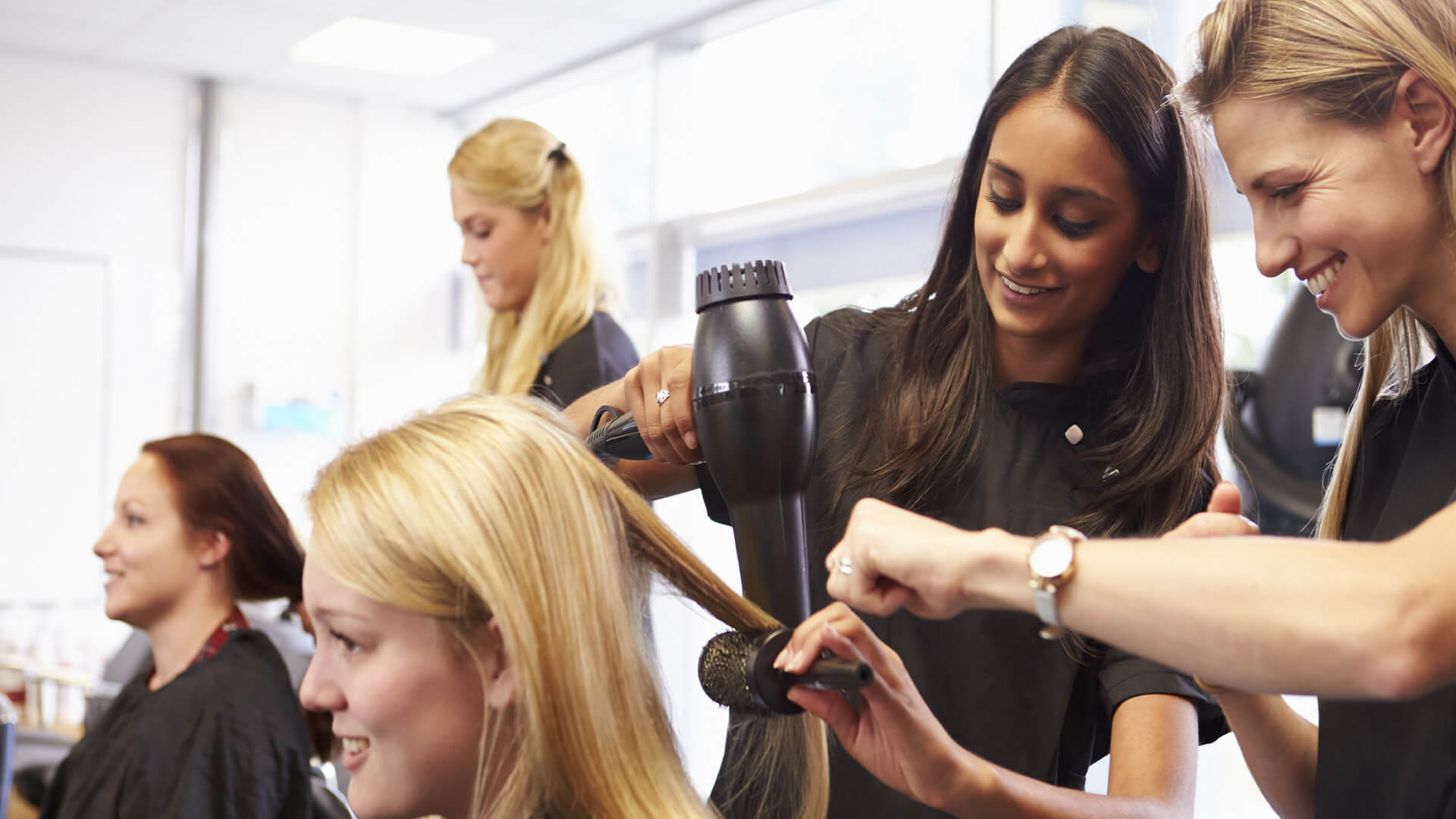 Women doing a female clients hair, with a round hair brush and a hair dryer