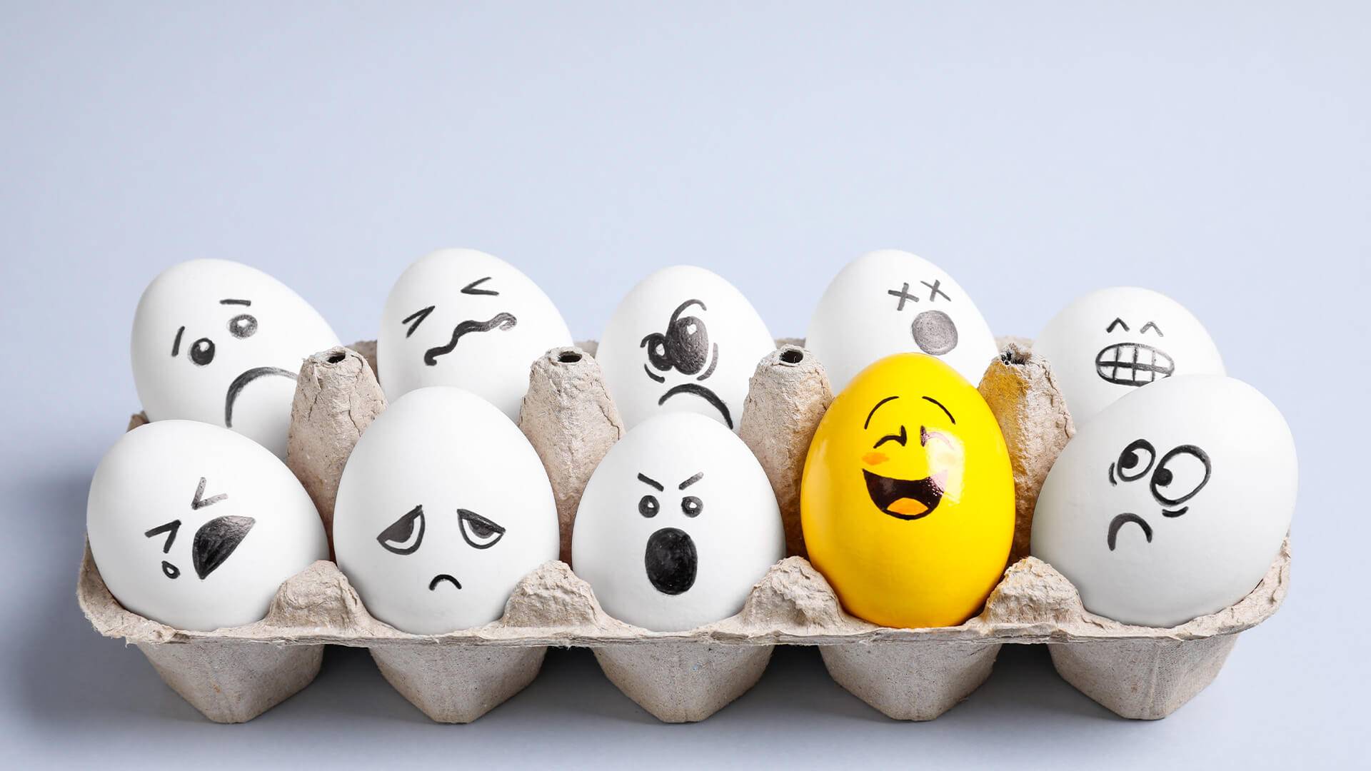 Yellow smiley egg among others with negative emotions in package on light background