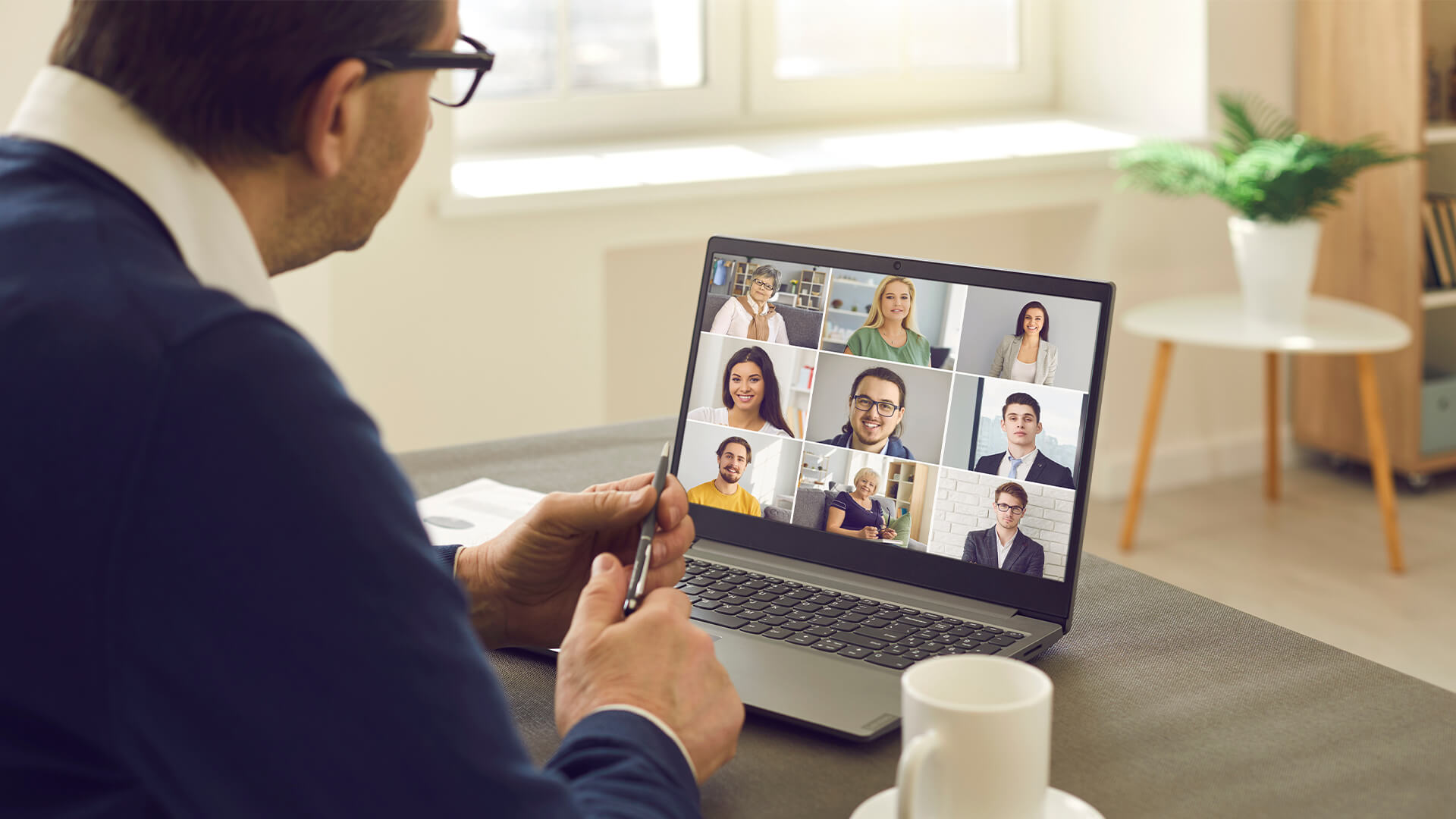 man sitting at table having virtual group meeting with team of co workers on laptop computer.