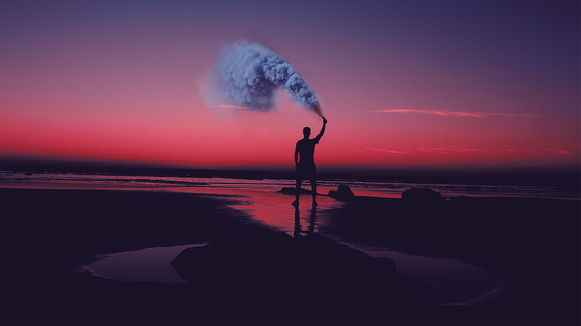 man standing by a pink sunset with smoke in his hand